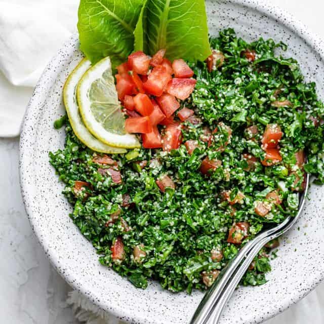Large bowl of kale tabbouleh salad with serving spoons on the inside of the bowl