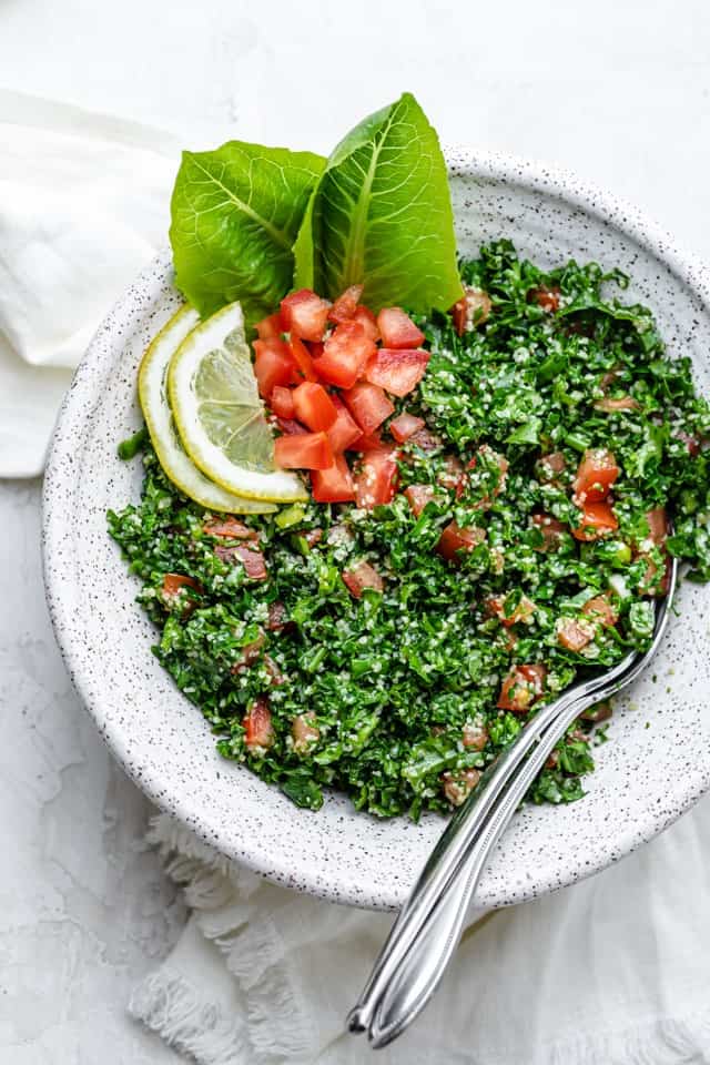 Large bowl of kale tabbouleh salad with serving spoons on the inside of the bowl