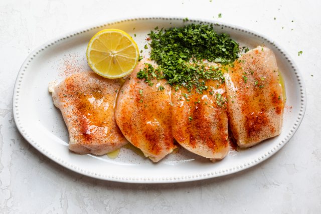 Chicken breast with seasoning, cilantro and half lemon on a plate