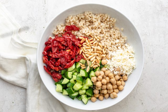 Ingredients to make the salad: pearl couscous, sundried tomatoes, cucumbers, chickpeas, feta cheese, pine nuts