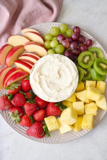Cream cheese fruit dip in the center of a round platter with fresh fruit around.