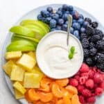 Cream cheese fruit dip surrounded by raspberries, clementines, pineapples, green apples, blueberries and blackberries