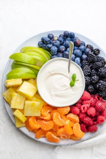 Cream cheese fruit dip surrounded by raspberries, clementines, pineapples, green apples, blueberries and blackberries