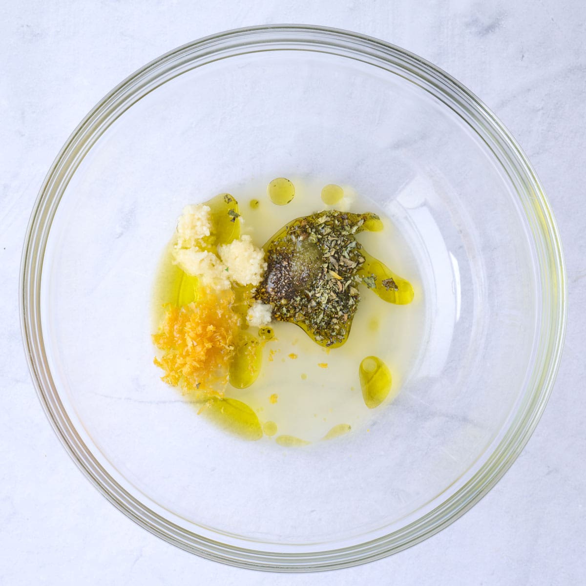 Olive oil, lemon juice, garlic, oregano, salt and pepper in a bowl before mixing.