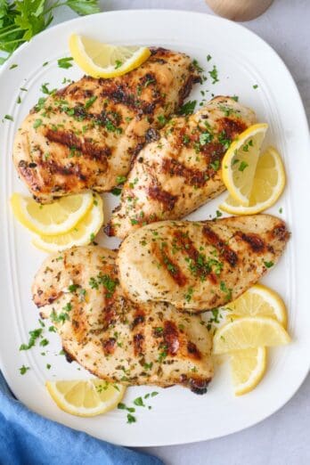Grilled chicken breasts on a platter garnished with parsley and lemon wedges.