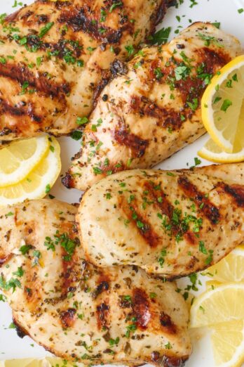 Grilled chicken breasts on a platter garnished with parsley and lemon wedges.