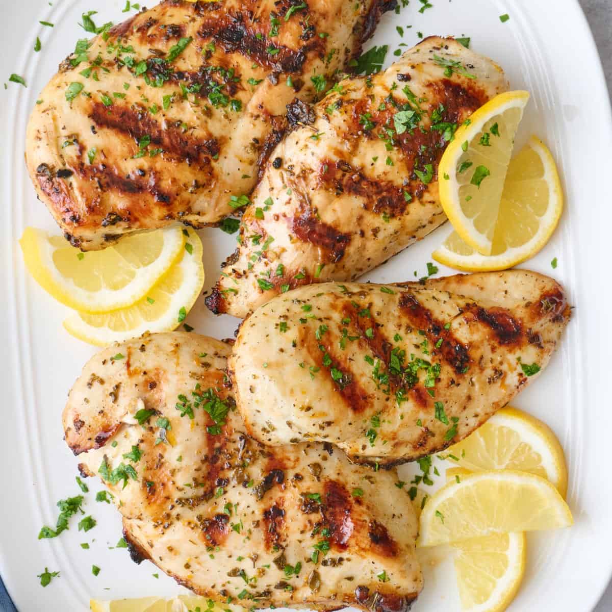 Grilled chicken breasts on a platter garnished with parsley and lemon wedges.