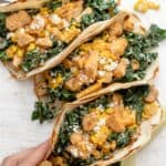 Mexican street tacos with kale, corn and chicken. Hand grabbing one taco