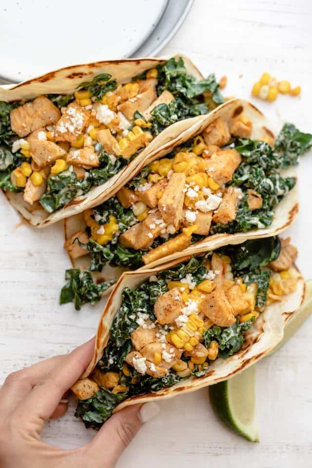 Mexican street tacos with kale, corn and chicken. Hand grabbing one taco