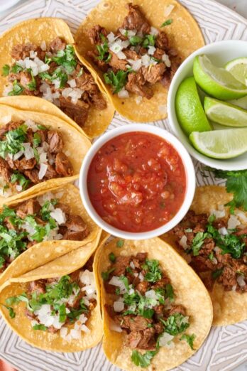 Mexican street tacos on a large round platter with salsa and limes.