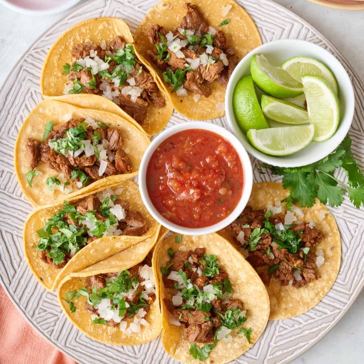 Mexican street tacos on a large round platter with salsa and limes.