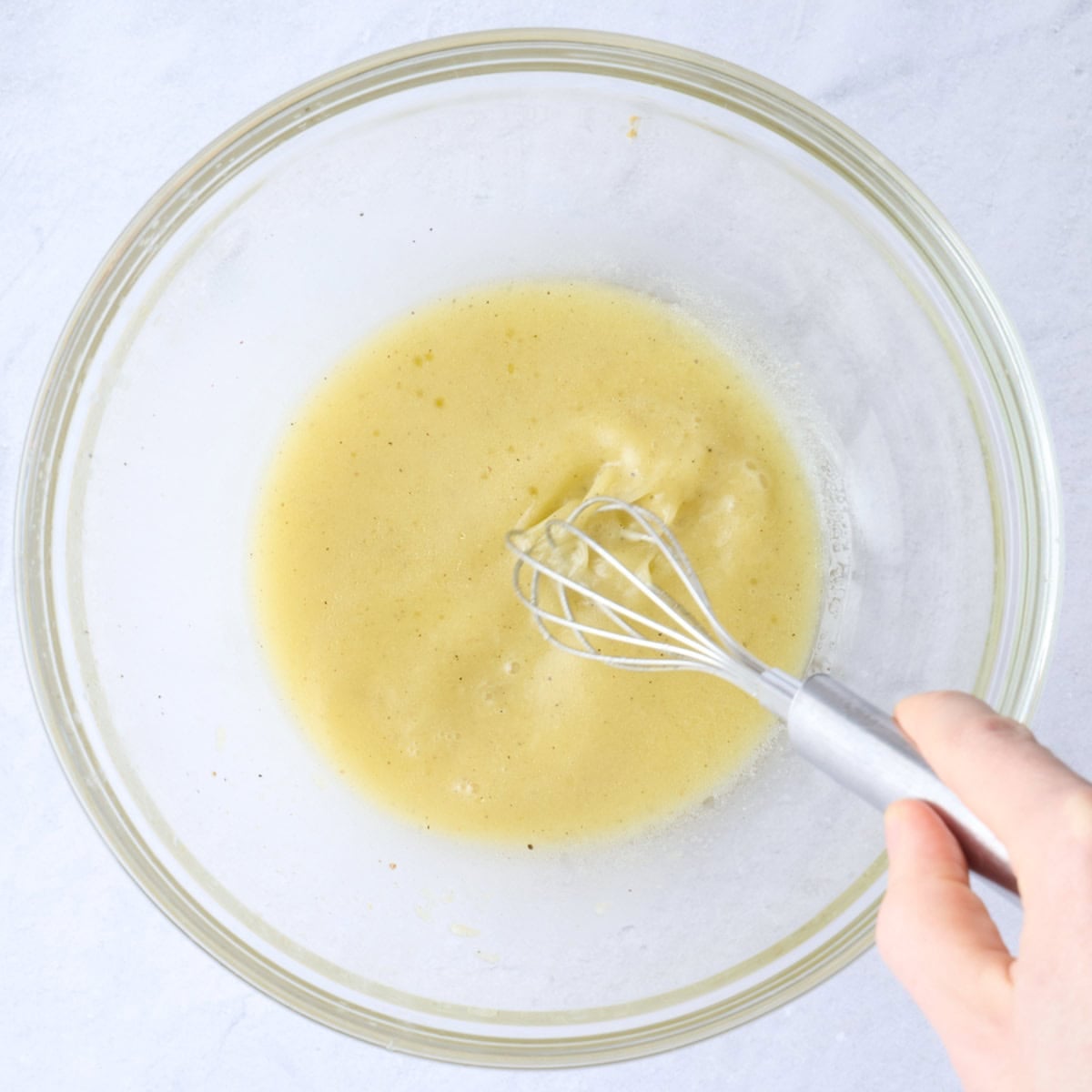 Dressing ingredients in a large bowl with a whisk whisking everything together.