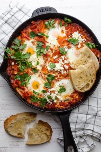 Shakshuka with Feta served with bread and cilantro in a cast iron skillet