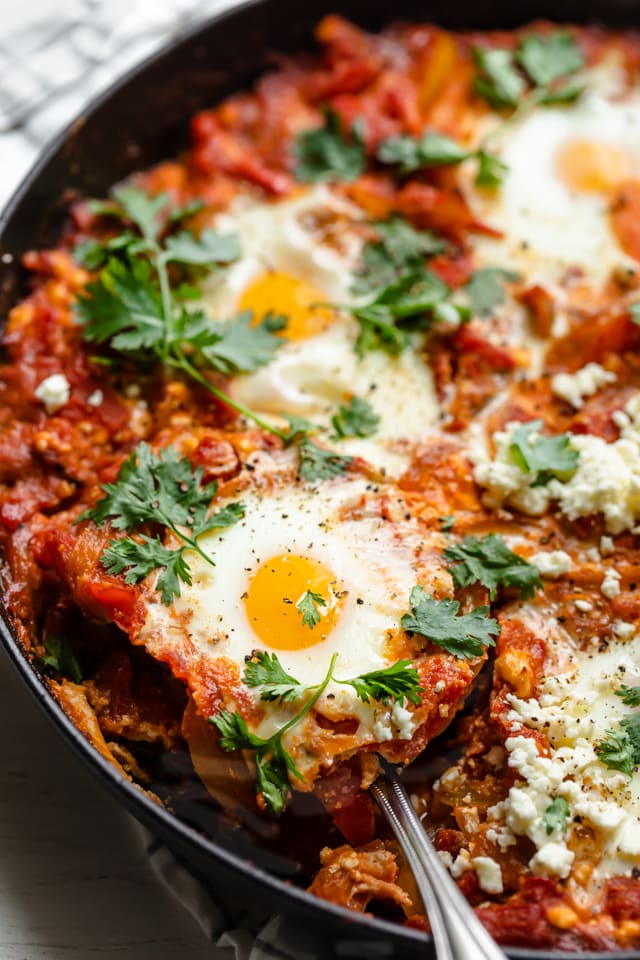 close up of spoon taking a portion out of a skillet of shakshuka