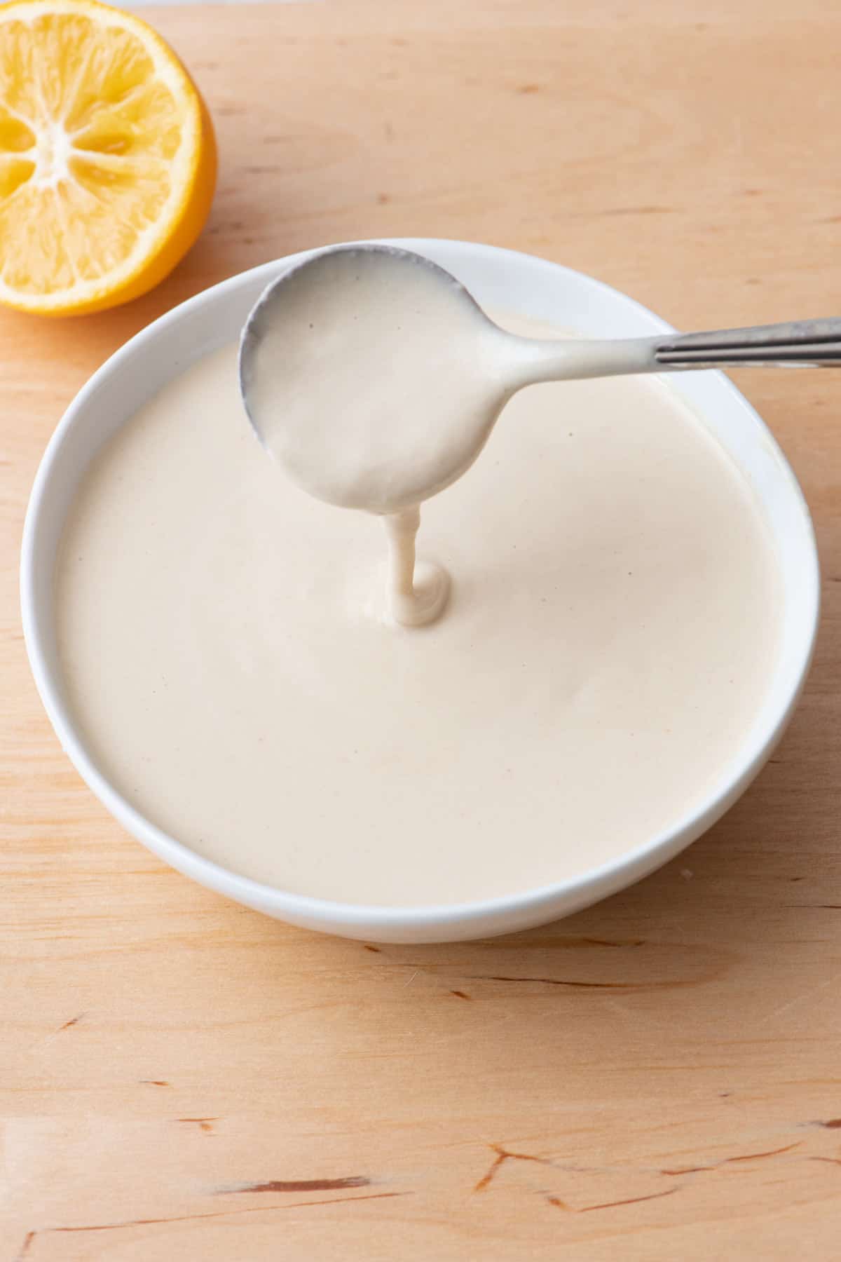 Spoon lifting up sauce from a bowl to show smooth, creamy, and runny consistency.