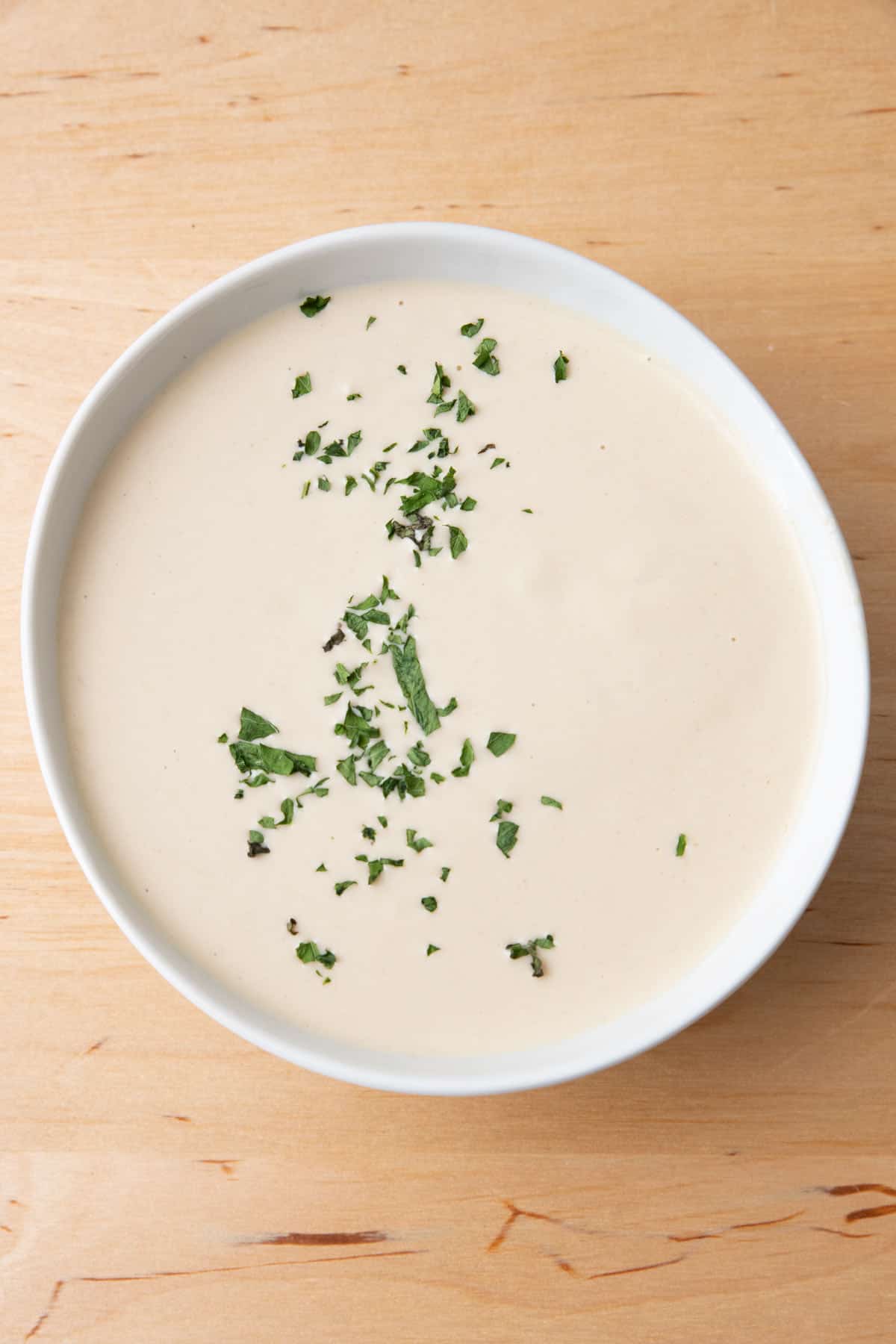 Bowl of tahini sauce with fresh chopped parsley garnish.