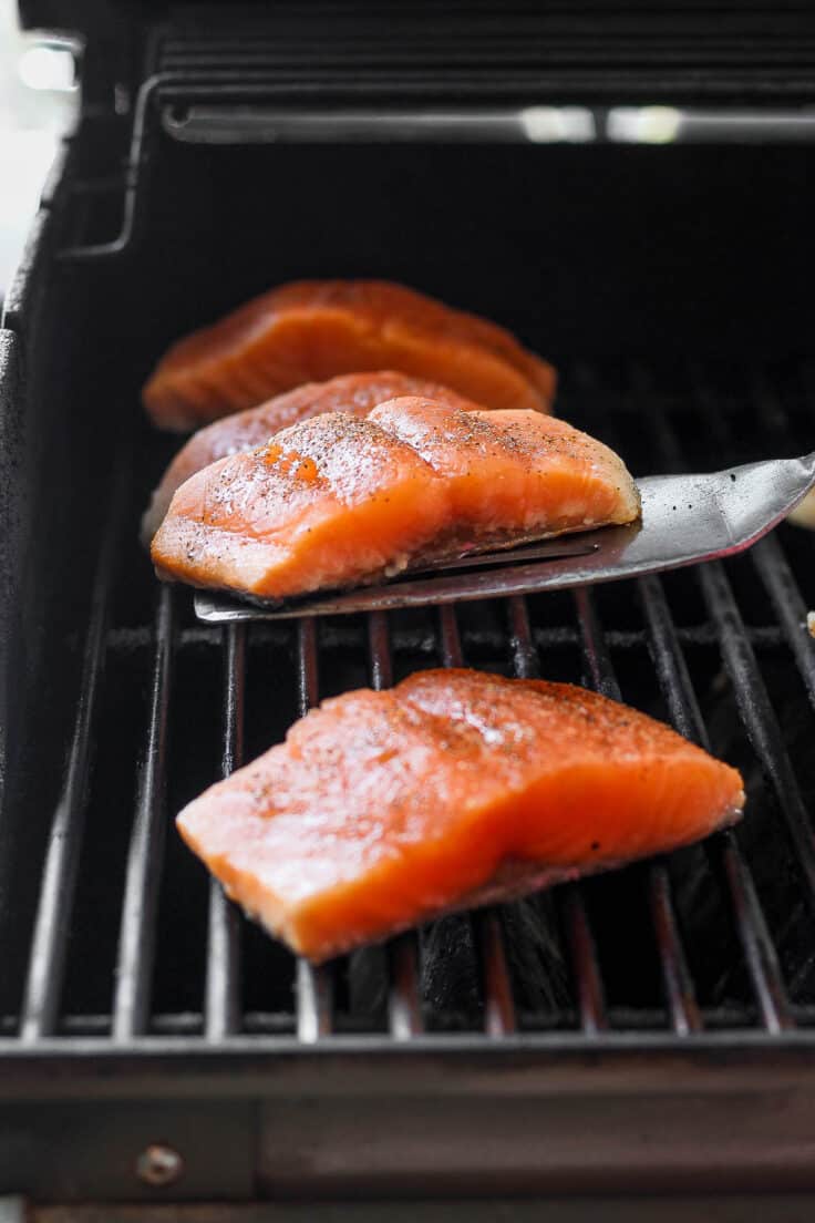 3 Salmon fillets on a grill with spatula under one before flipping it