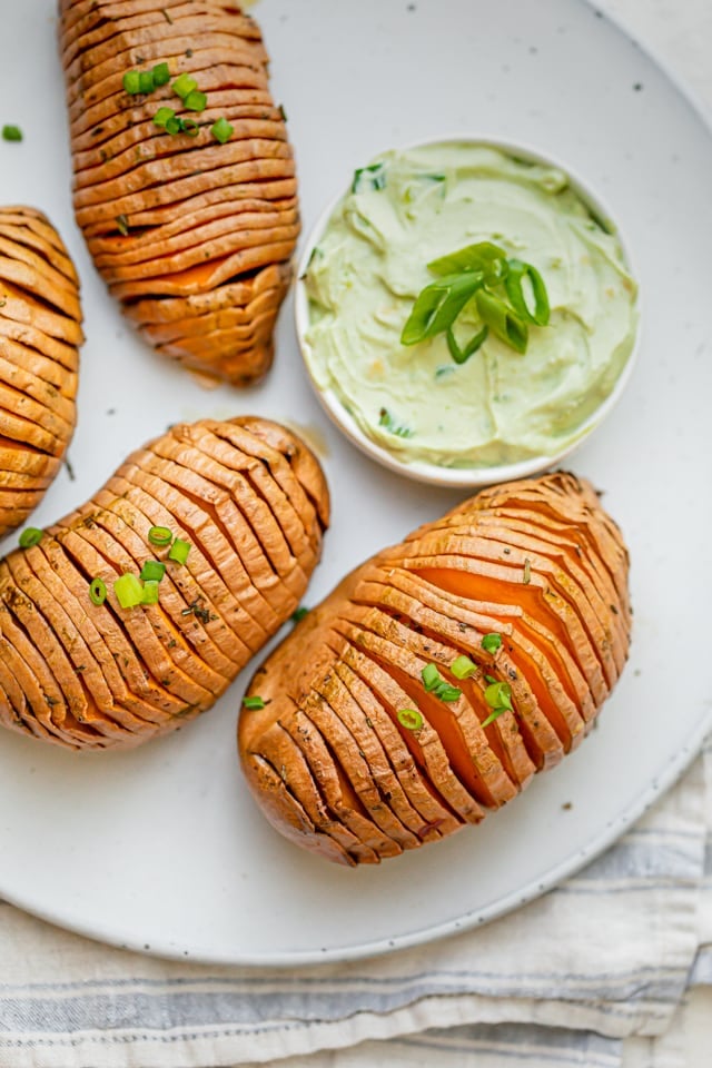 Baked hasselback sweet potatoes on a white plate served with avocado yogurt sauce