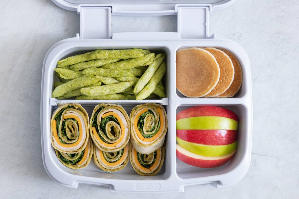 Lunchbox with turkey pinwheels, apples, mini pancakes and green peans