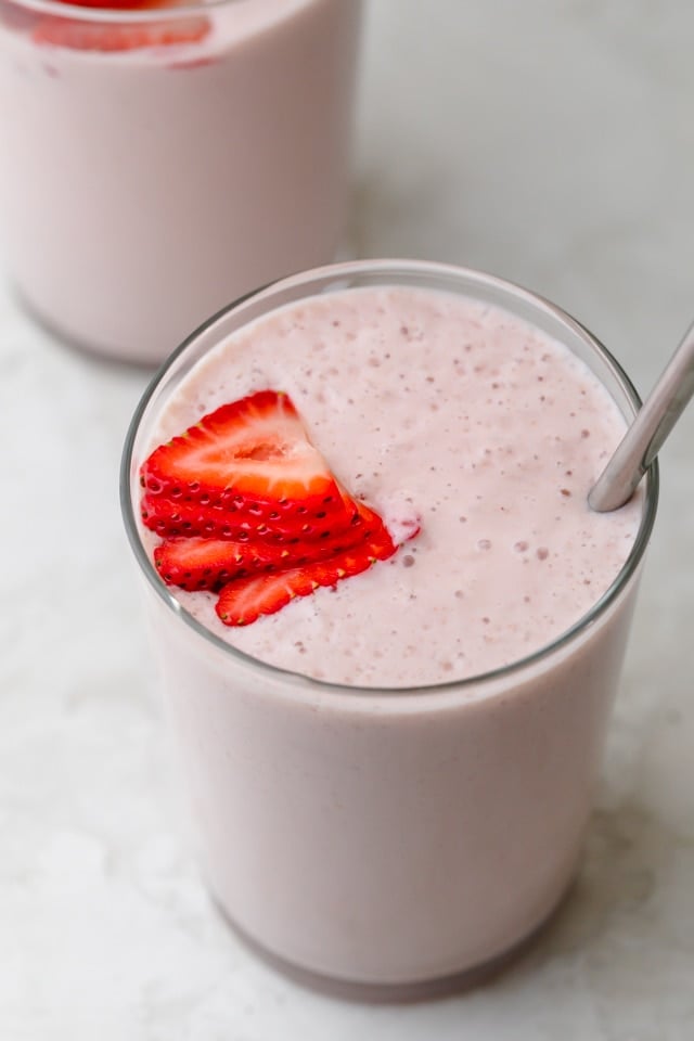 Tall glass of strawberry banana smoothie with a straw inside