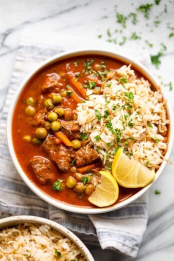 A bowl of peas and carrots stew garnished with lemon wedges