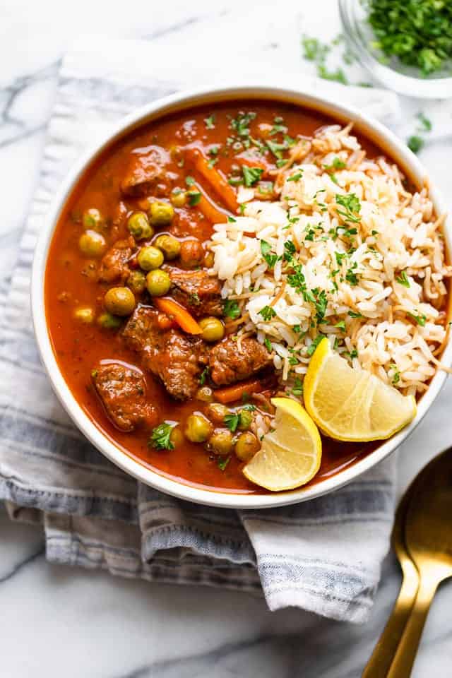 A bowl of peas and carrots stew served with lemon wedges