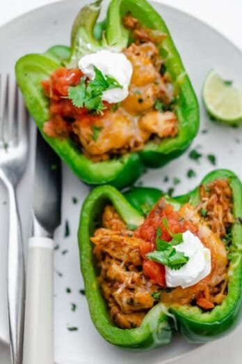 Chicken stuffed peppers on a white plate topped with pico de gallo and sour cream