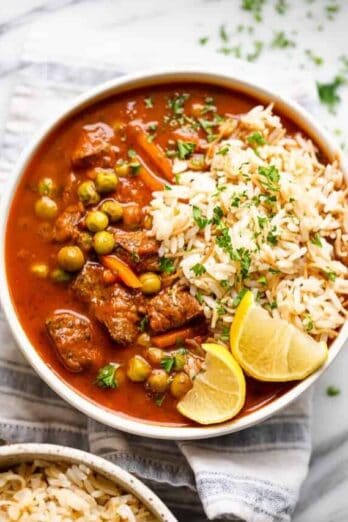 A bowl of peas and carrots stew served with lemon wedges