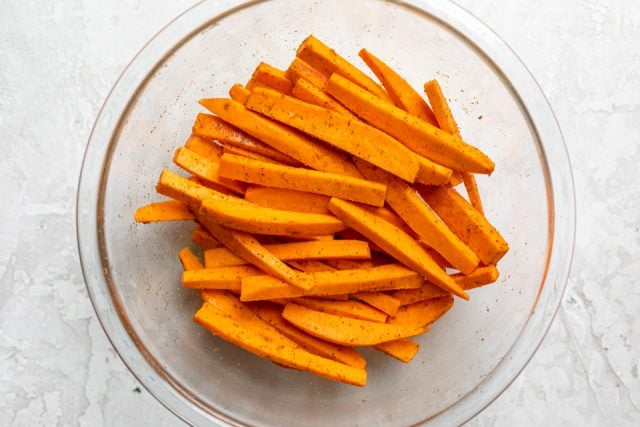 Sweet potatoes sliced in a bowl with olive oil and seasoning