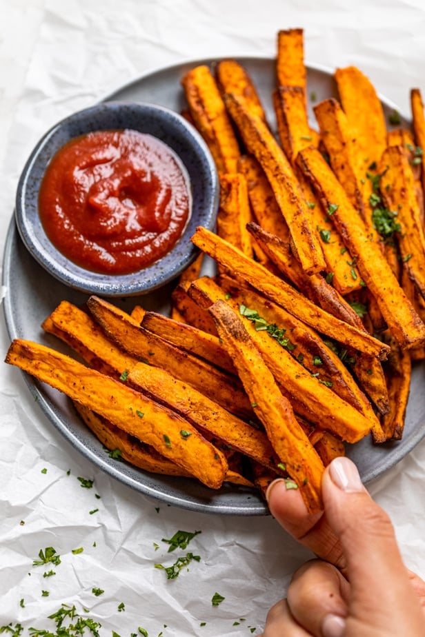 Grabbing one fry from plate of sweet potato fries