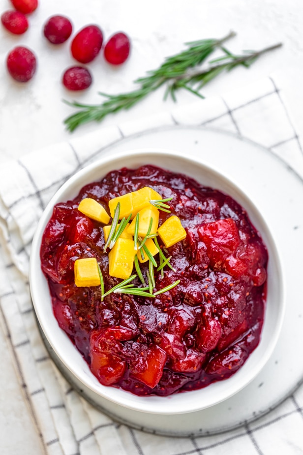 Small bowl of the finished cranberry mango sauce topped with mangos and rosemary