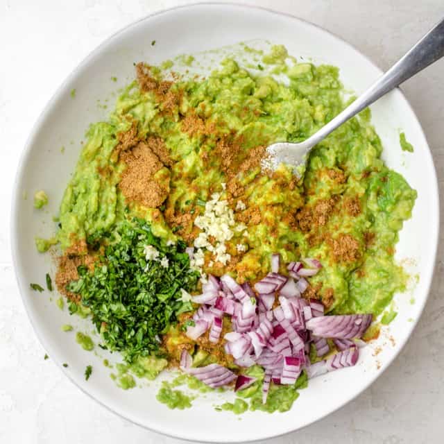 Guacamole ingredients added to the bowl with the avocados, before mixing.