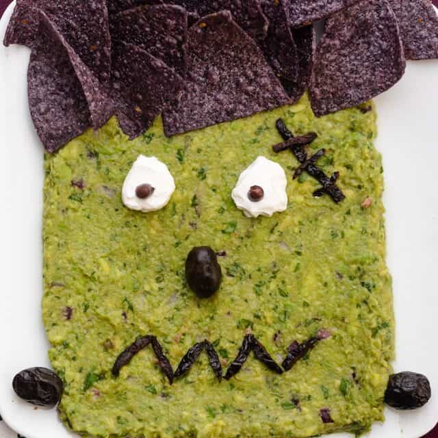 Frankenguac Halloween guacamole decorated with tortilla chips, olive and sour cream