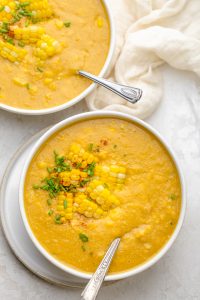 Two bowls of vegan corn chowder with spoons inside