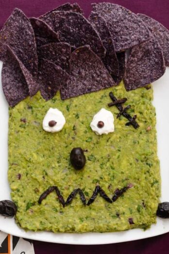 Frankenguac Halloween guacamole decorated with tortilla chips, olive and sour cream