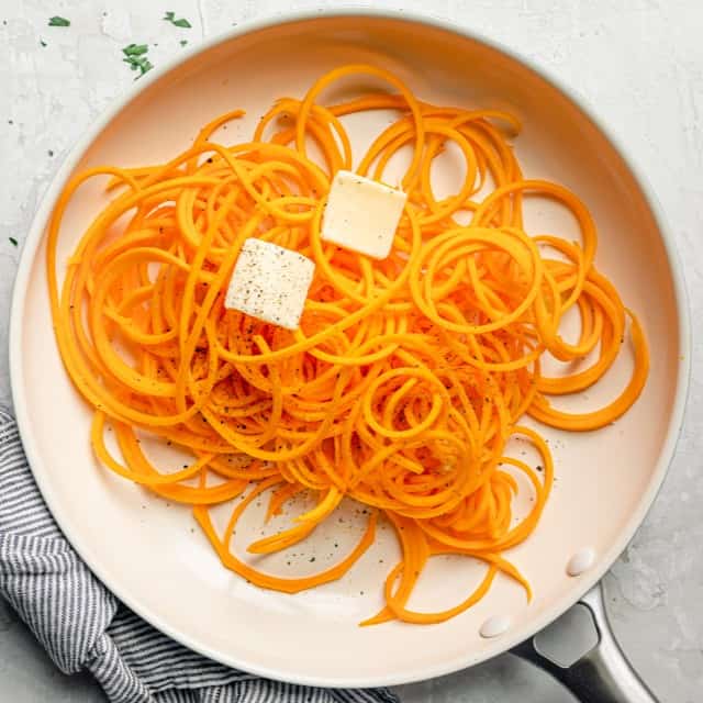 Noodles inside of a sautee pan with seasoning and butter.