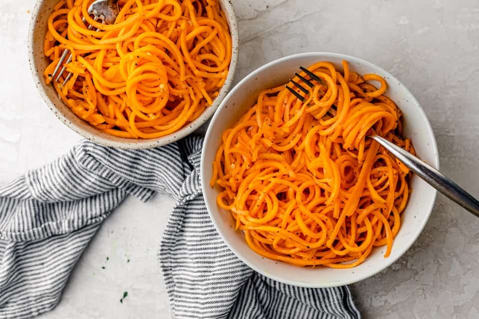 Two bowls of cooked butternut squash noodles with utensils in each.