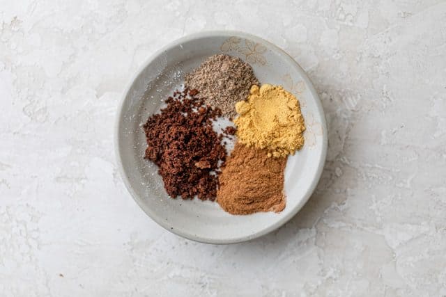 Bowl of the four spices used in the recipe: cloves, ginger, cinnamon and cardamom