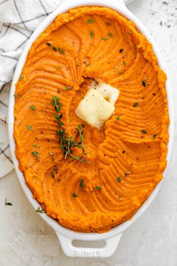 Large oval casserole dish with healthy mashed sweet potatoes topped with butter and thyme