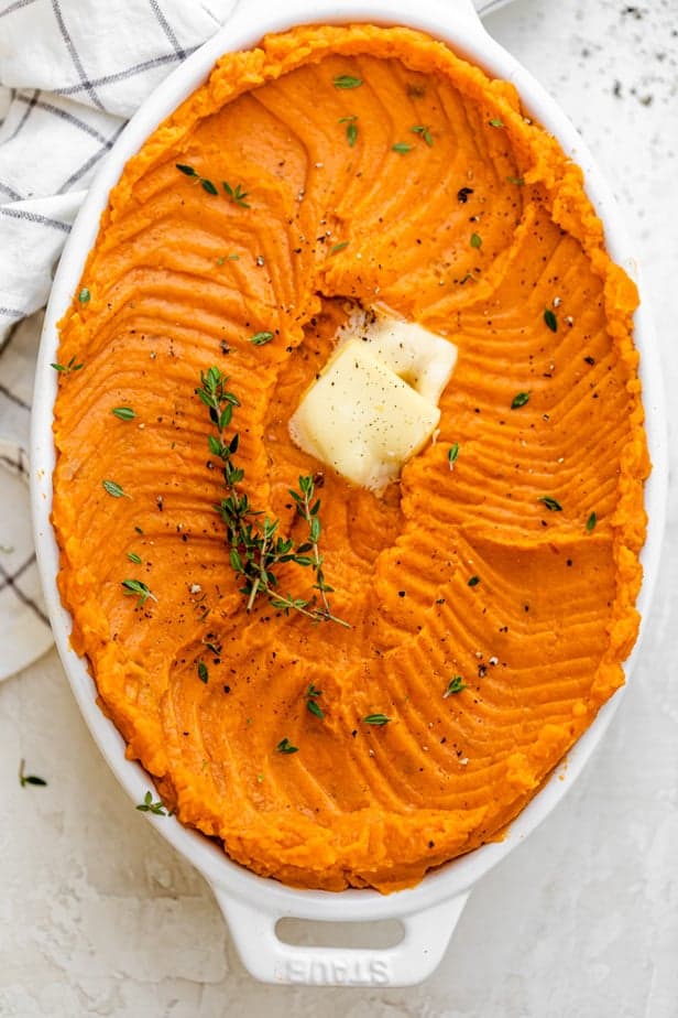 Large oval casserole dish with healthy mashed sweet potatoes topped with butter and thyme