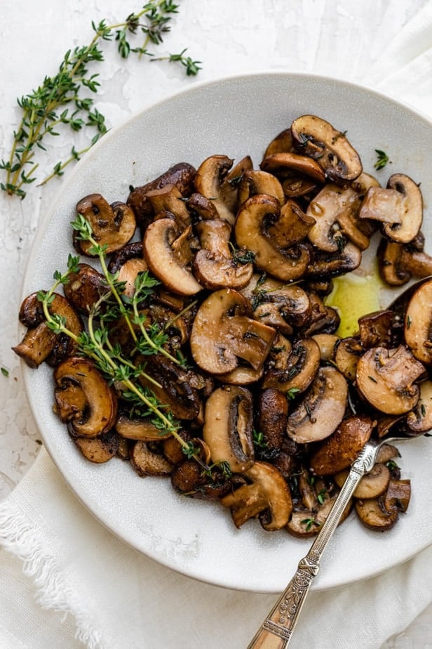 Spoon serving the sauteed mushrooms on a white plate