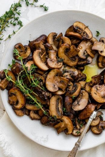 Spoon serving the sauteed mushrooms on a white plate