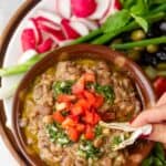 Pita dipping into ful medames bowl surrounded by vegetables