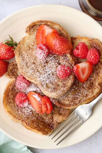Vegan French Toast on a plate topped with strawberries, with more toppings and another plate of the french toast surrounding.