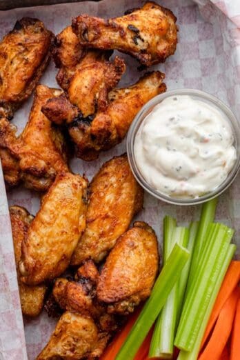 A tray of air fryer chicken wings with dipping sauce and celery and carrot sticks nearby.