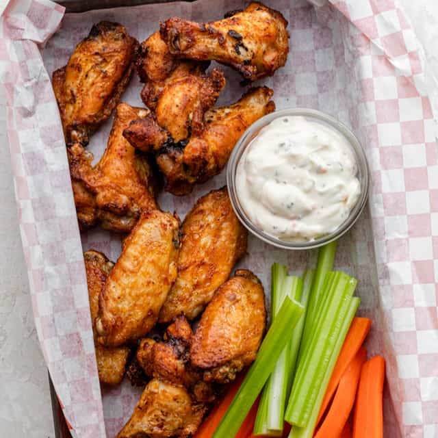 A tray of air fryer chicken wings with dipping sauce and celery and carrot sticks nearby.