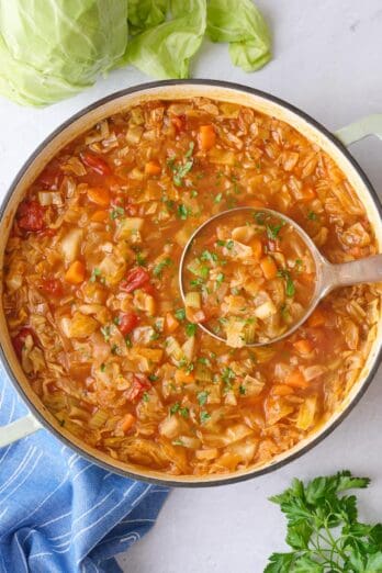 Cabbage soup in a pot with ingredients nearby.