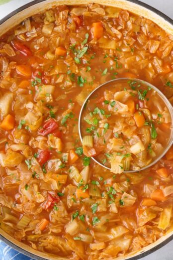 Cabbage soup in a pot with ingredients nearby.