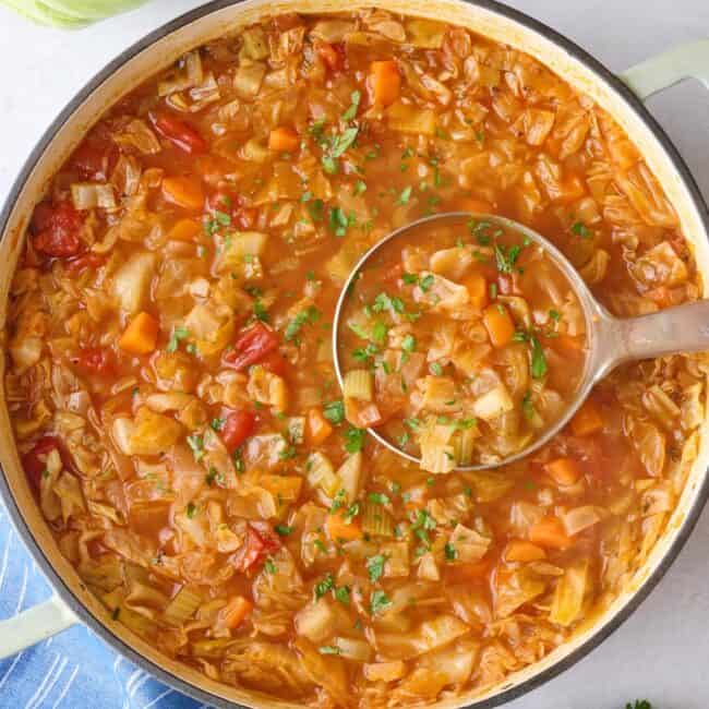 Cabbage soup in a pot with ingredients nearby.