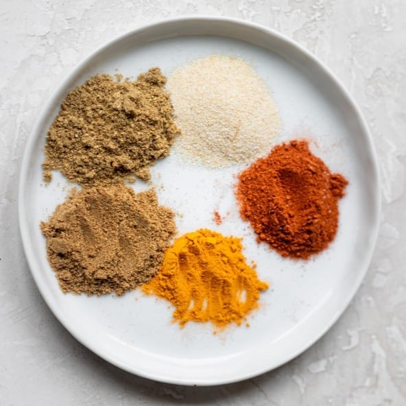 The seasonings to make pan seared chicken thighs separated on a plate.